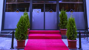 The exterior of Hotel Marina with a red carpet entrance, potted plants, and multiple flags displayed outside. - Marina Hotel (Izmir)