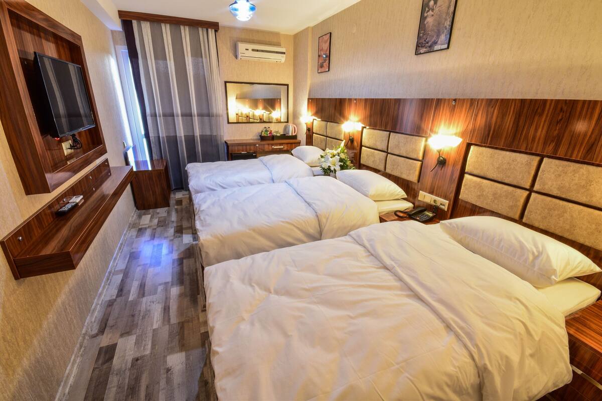 A hotel room with a large bed, a TV, a mirror, and a bedside table with a lamp.