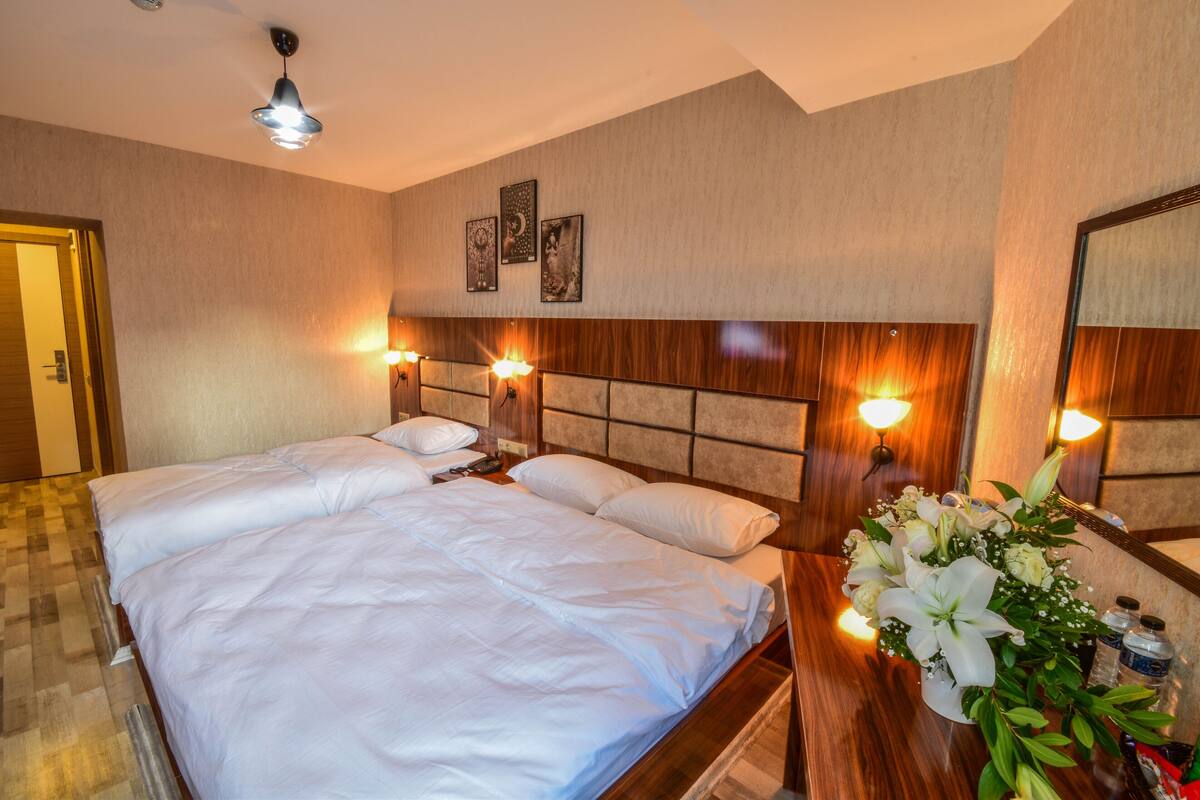 A hotel room with a large bed, two bedside tables, a wooden headboard, wall-mounted lights, and a mirror.