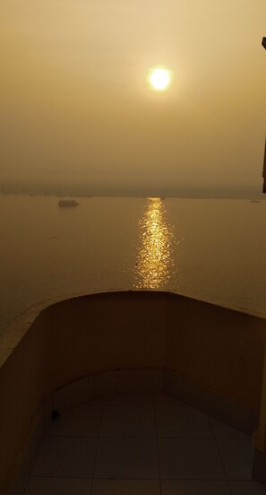 A sunset over a body of water with a boat in the distance. - Dwivedi Hotels Hotel Elena (Varanasi)