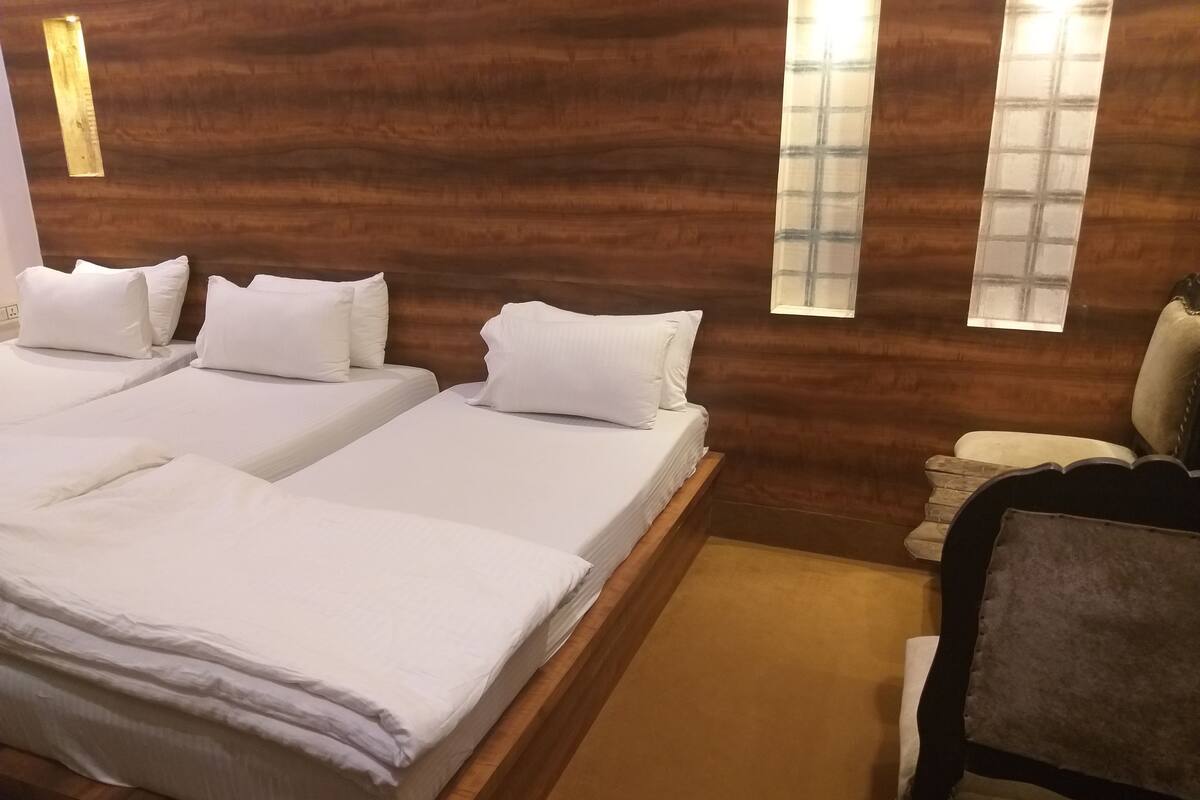 A room with two beds, wooden headboard, and a small seating area with a chair.