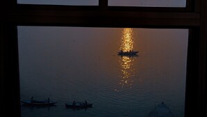 Un coucher de soleil observé à travers une fenêtre ornée d’une arche décorative, se reflétant sur l’eau avec des bateaux.