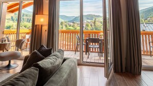 Une pièce chaleureuse avec un plafond en bois, une tête de cerf accrochée au mur, un canapé et un balcon offrant une vue sur les montagnes.