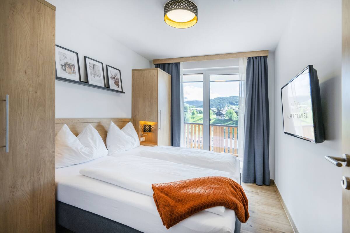 Een hotelkamer met een groot bed, een houten kledingkast, een wandgemonteerde televisie en een balkon met uitzicht op het landschap.