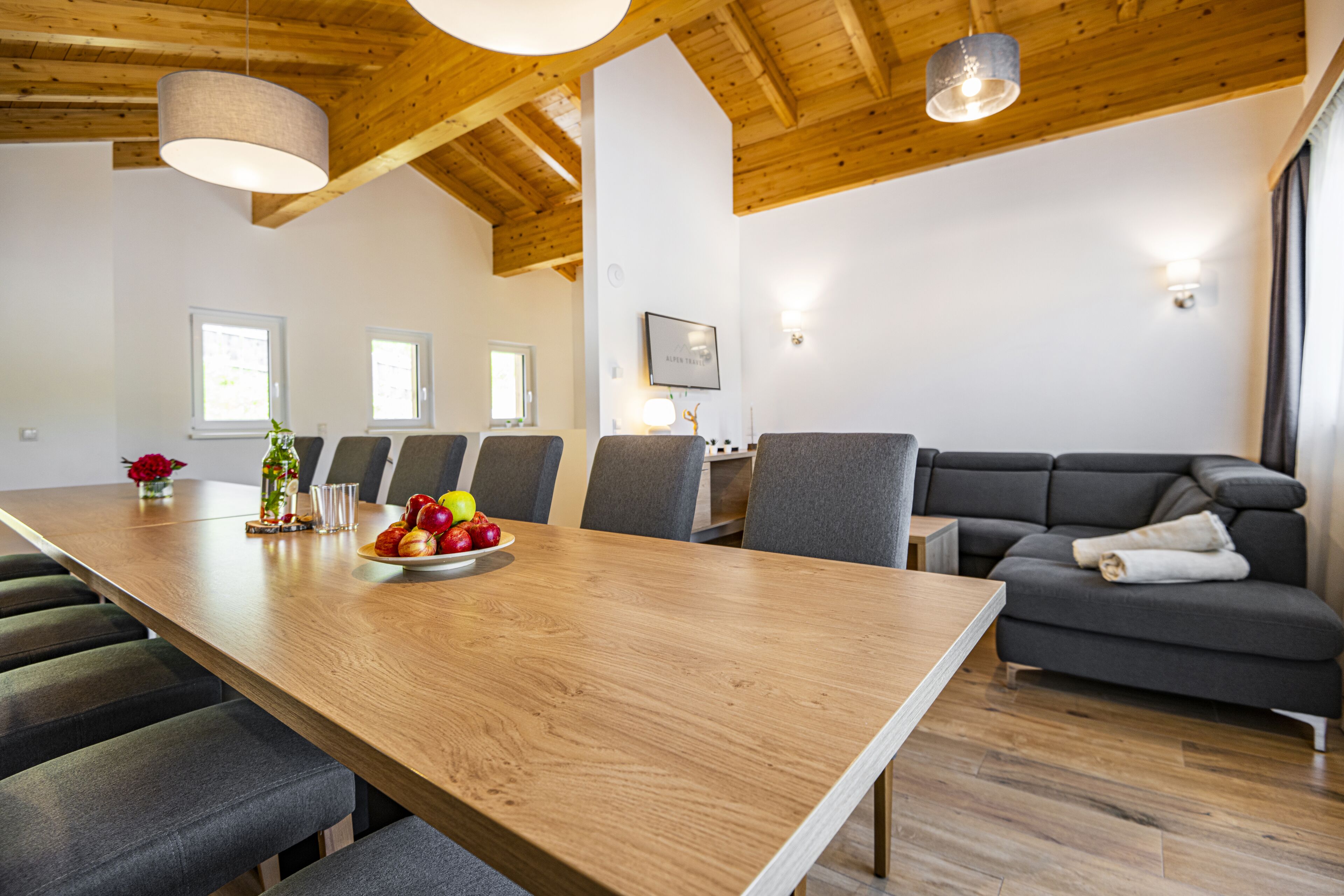A modern dining area with a wooden table, grey upholstered chairs, and a grey sofa.
