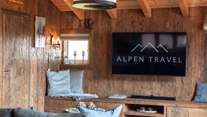 Un intérieur en bois avec un téléviseur diffusant l’émission « ALPEN TRAVEL », un canapé et un meuble en bois.