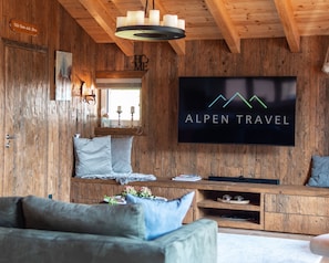 Un interior de madera con un televisor mostrando 'ALPEN TRAVEL', un sofá y un armario de madera.