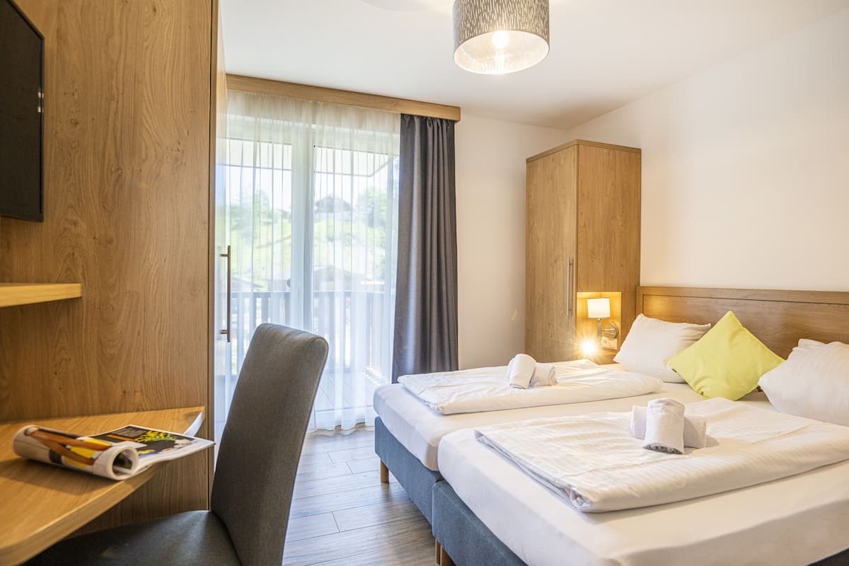 Een hotelkamer met twee bedden, een bureau, een stoel en een groot raam met gordijnen.