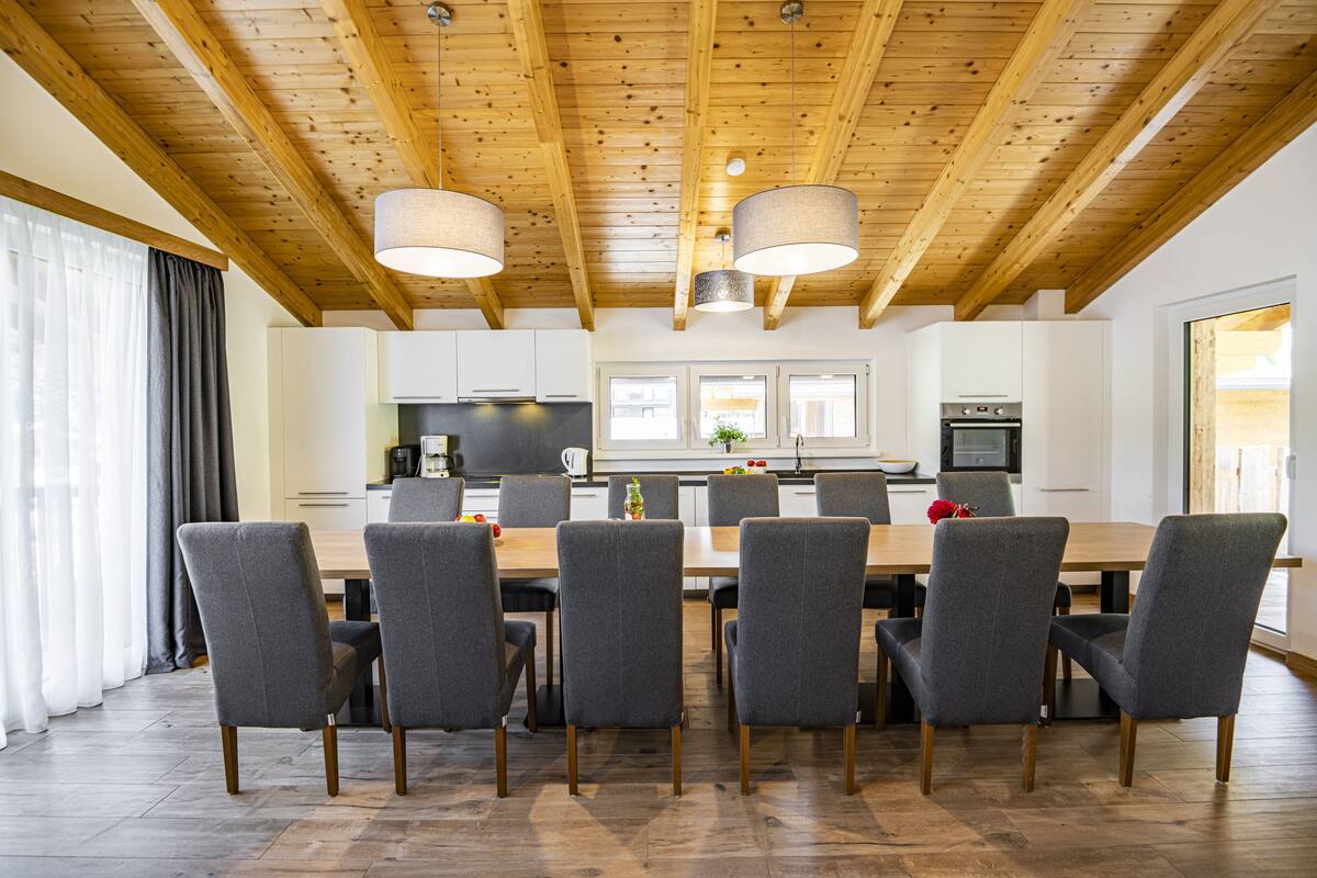 Een moderne eetruimte met een houten plafond, grijze bekleden stoelen en een centrale tafel.