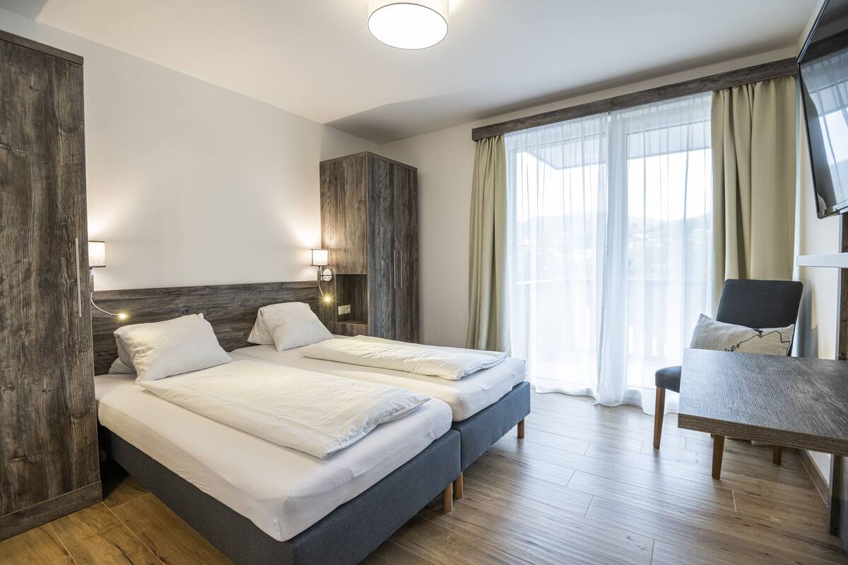 Een moderne hotelkamer met twee bedden, een houten garderobe, een bureau met stoel, en een televisie.