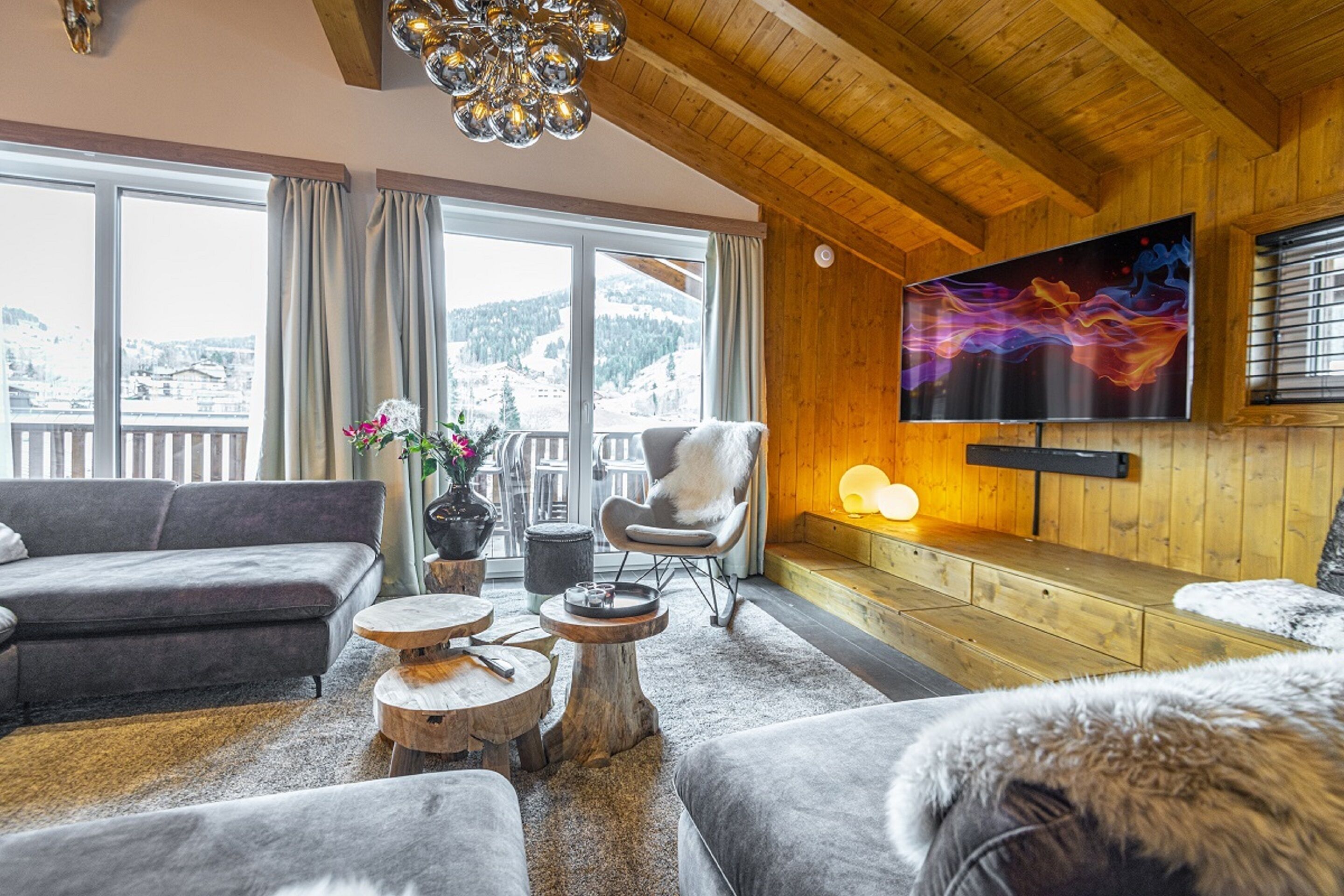 Un salon chaleureux avec une grande télévision, des meubles en bois et une vue sur des montagnes enneigées.