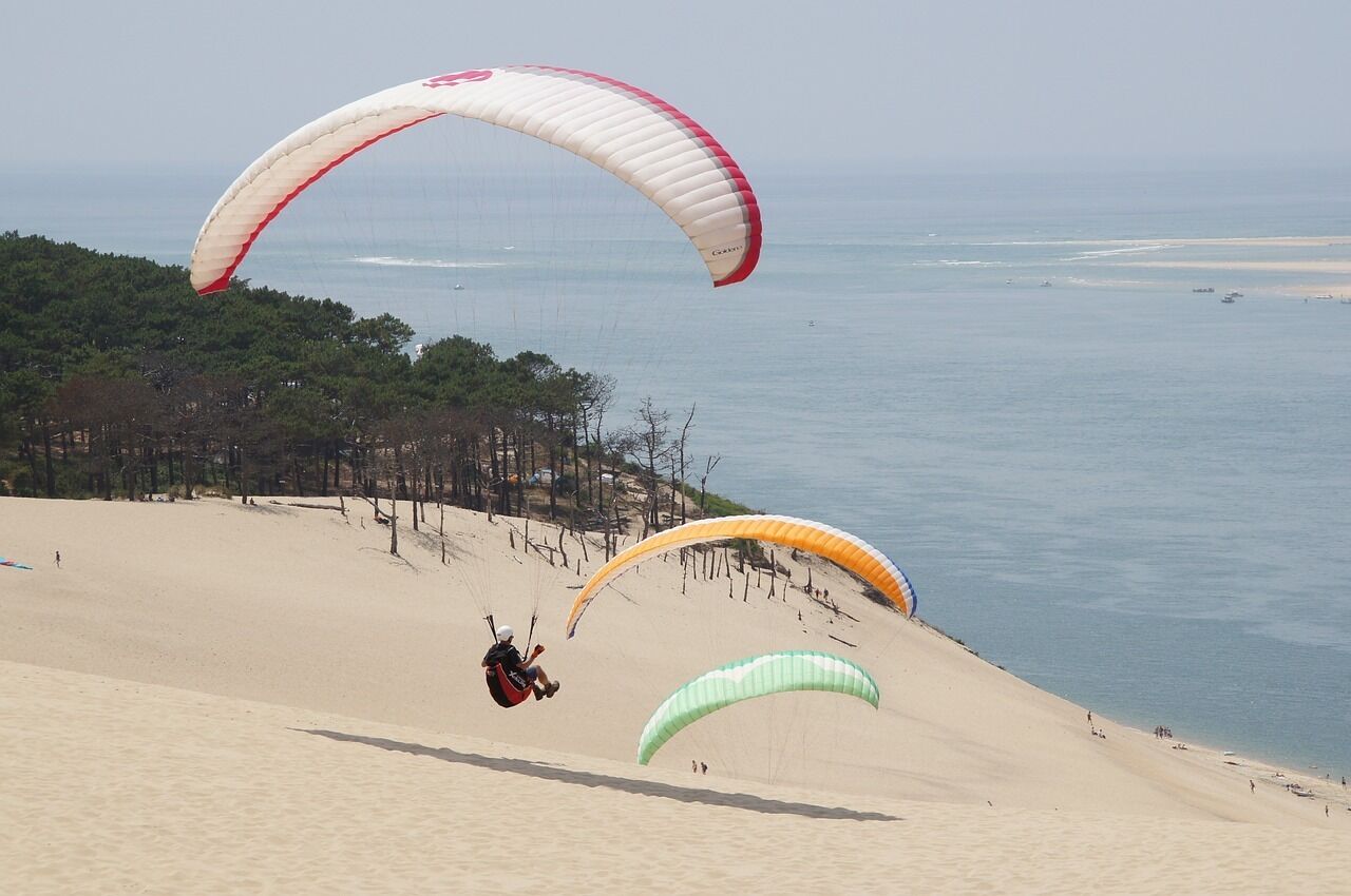 Une plage avec des dunes de sable et une personne pratiquant le parapente.