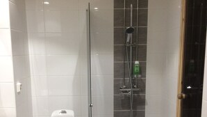 A bathroom with a toilet, a glass-enclosed shower, and a tiled floor. - Kotimaailma Apartments Siljotie (Rovaniemi)