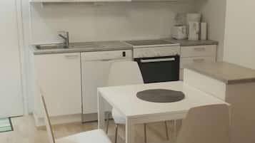 Cocina compacta con armarios blancos, un microondas, una estufa y una mesa de comedor con dos sillas.