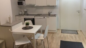 A compact kitchen with white cabinets, a microwave, a coffee maker, and a sink. There is a dining table with two chairs and a small potted plant. - Kotimaailma Apartments Siljotie (Rovaniemi)