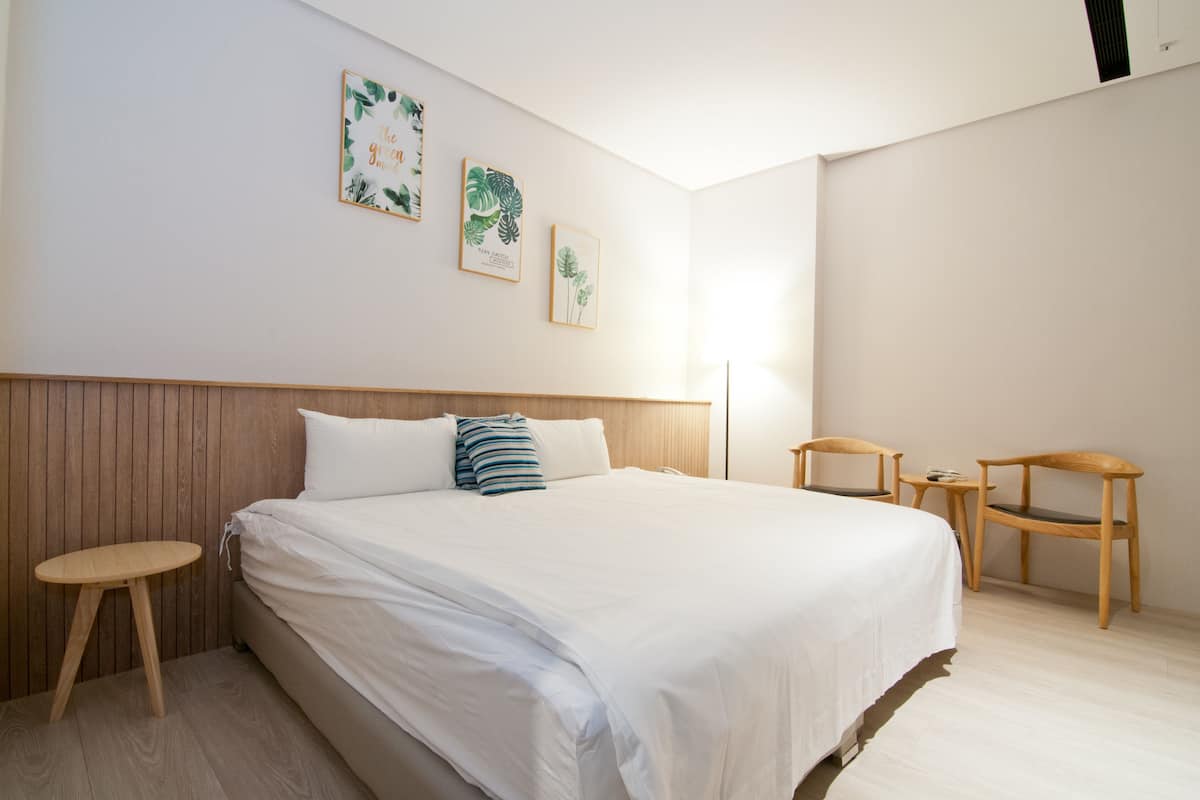 A modern bedroom with a large bed, two wooden chairs, a small table, and three framed botanical prints on the wall.
