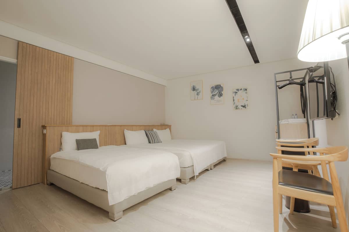 A bedroom with two beds, a wooden wardrobe, a mirror, and a chair.