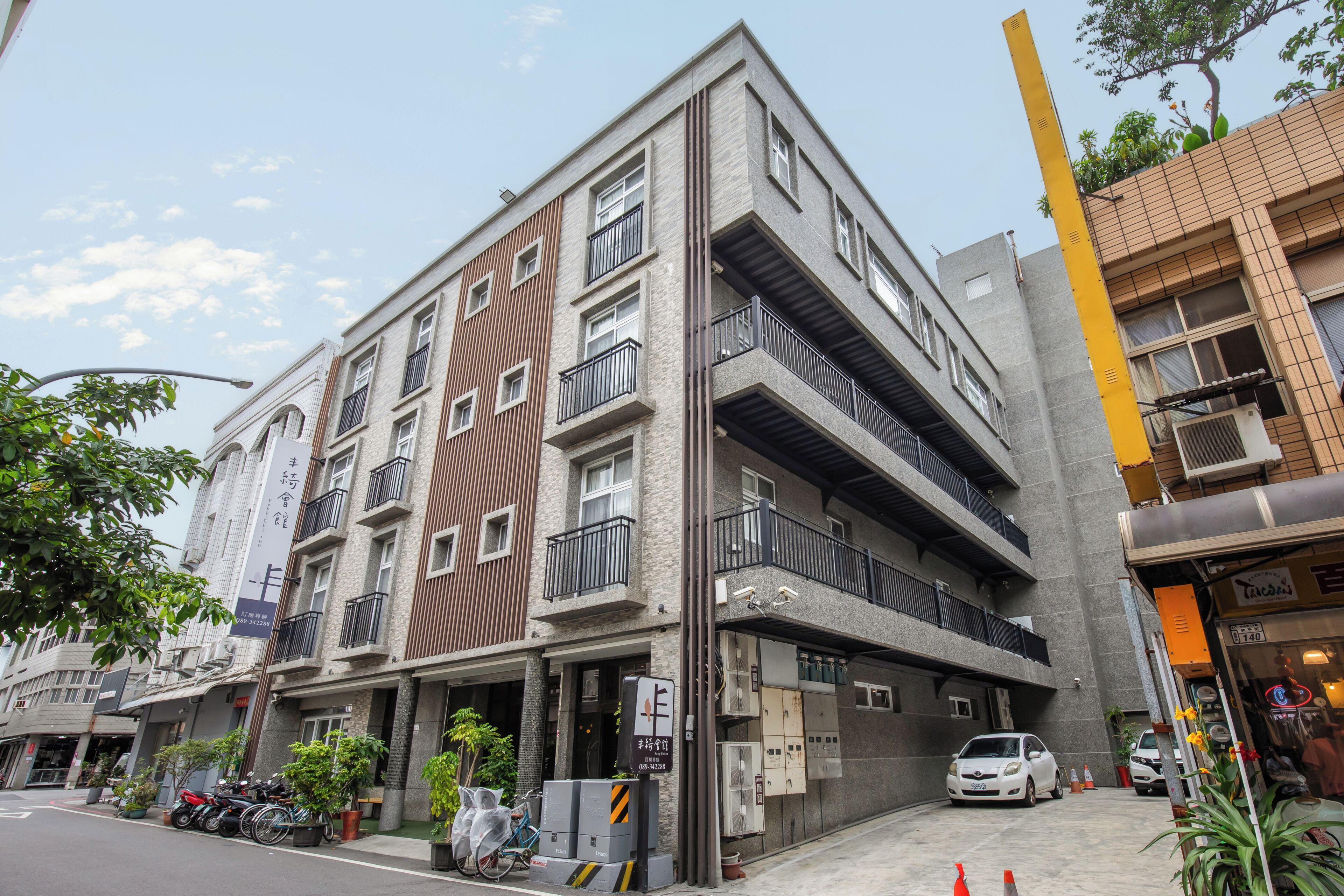 Un edificio de varios pisos con balcones, zona de estacionamiento y escaparates.