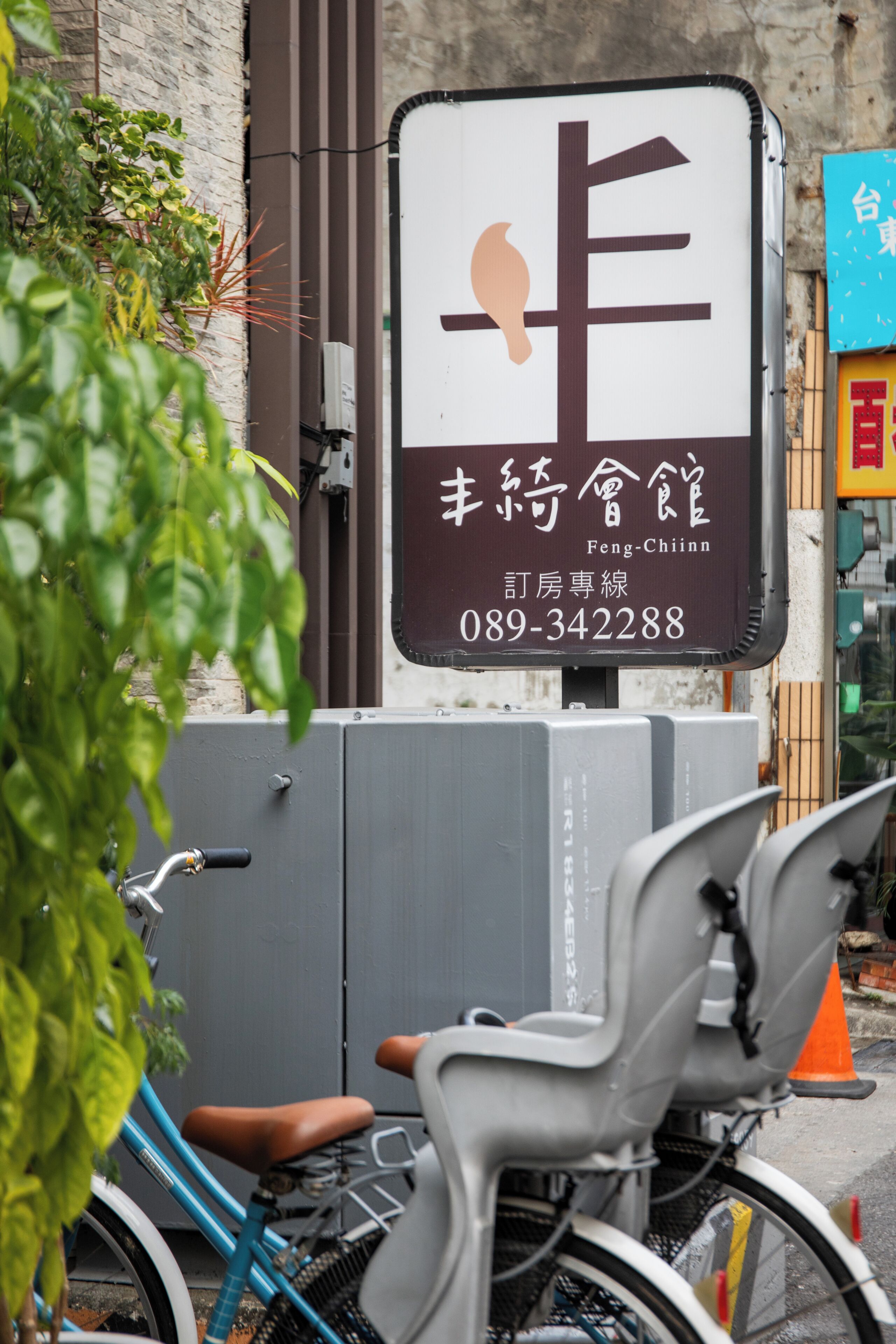 A sign with Chinese characters and a phone number, a bicycle, and a grey chair.