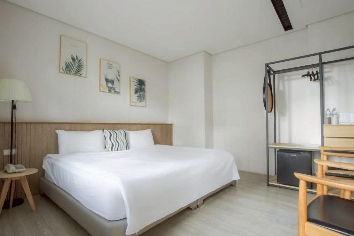 Habitación de hotel con cama, mesita de noche con lámpara, una silla y ventana con vistas.