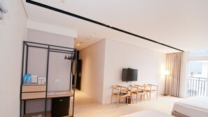 Ein Hotelzimmer mit einem Bett, einem Schreibtisch mit Stühlen, einem Fernseher und einem Kleiderschrank mit darin hängender Kleidung.