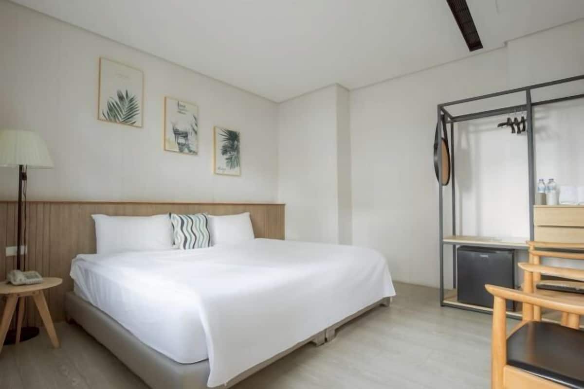A hotel room with a bed, a desk, a chair, a lamp, and wall art.