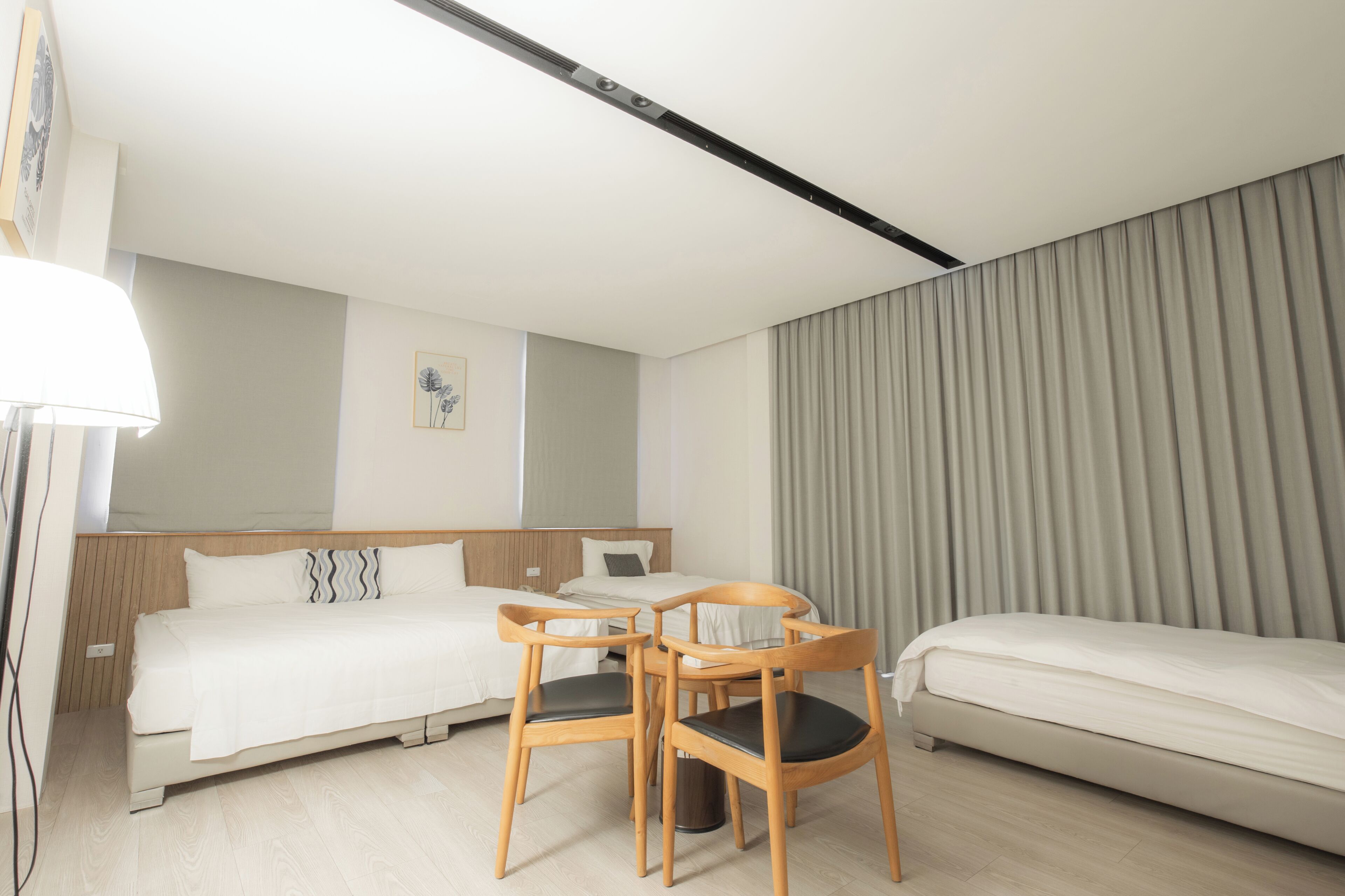 Une chambre d’hôtel avec un lit, deux chaises en bois, une petite table, une lampe, un tableau au mur et un rideau.