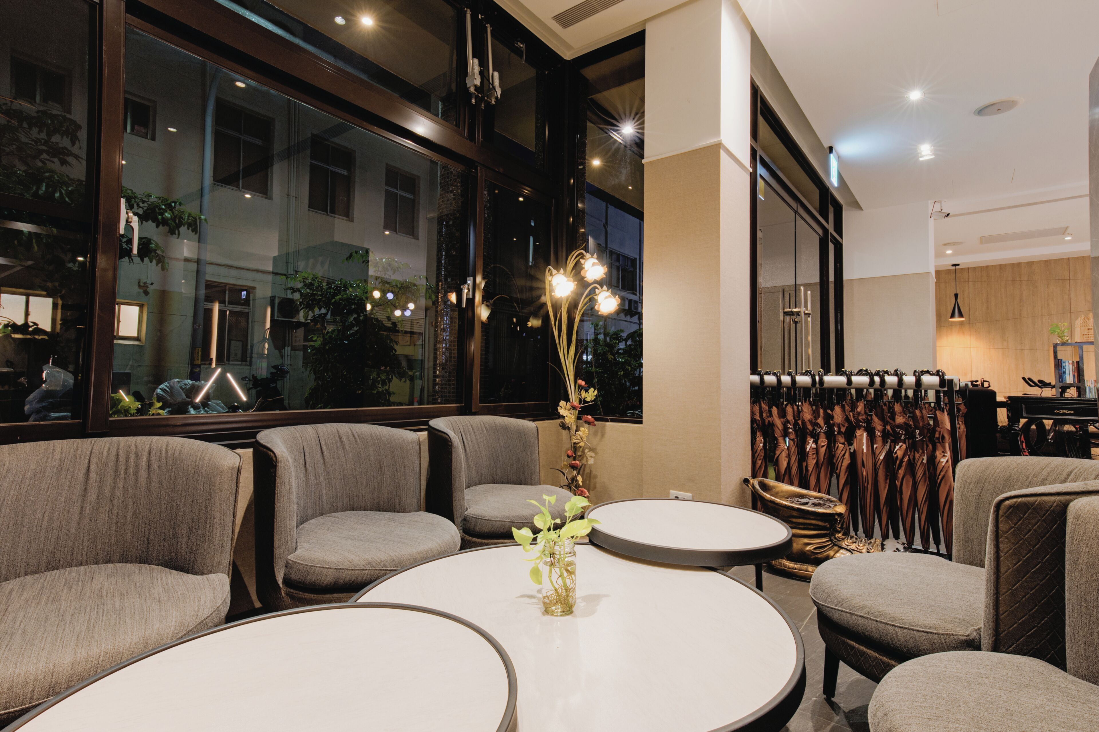 A modern interior with round tables, grey upholstered chairs, and a decorative vase with plants.