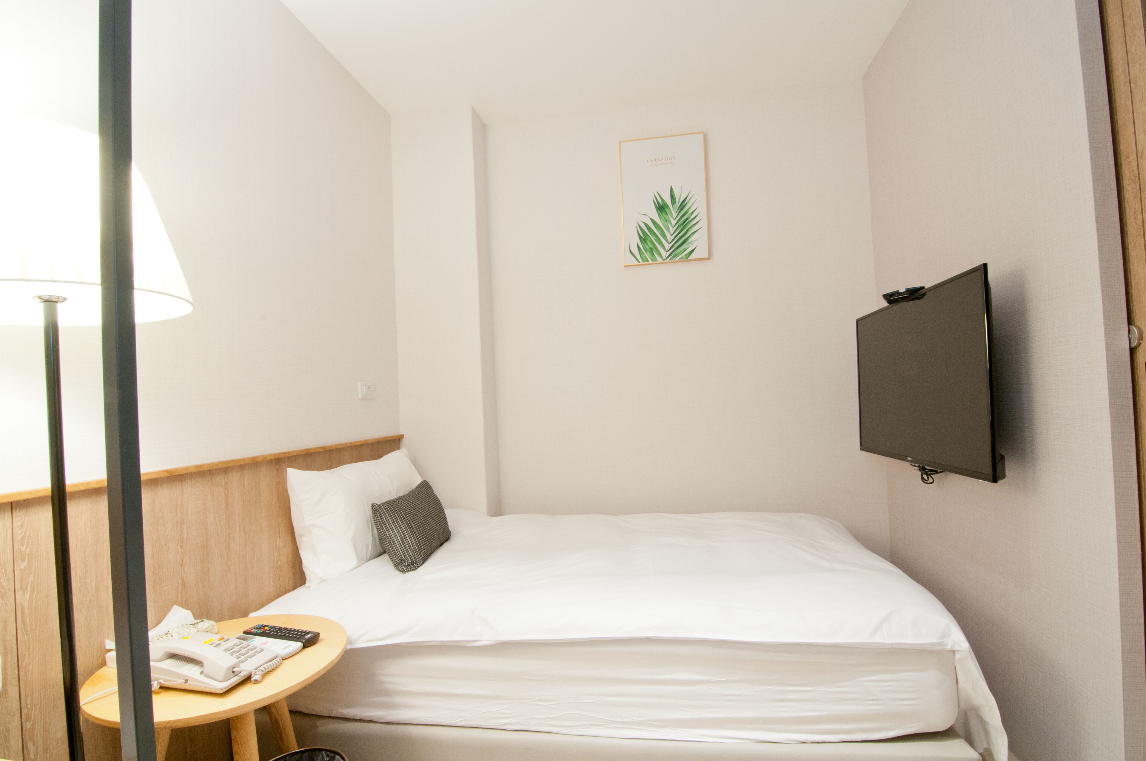 Une chambre d’hôtel comprenant un lit, une table de chevet avec un téléphone et une télécommande, un téléviseur fixé au mur et un tableau encadré accroché au mur.
