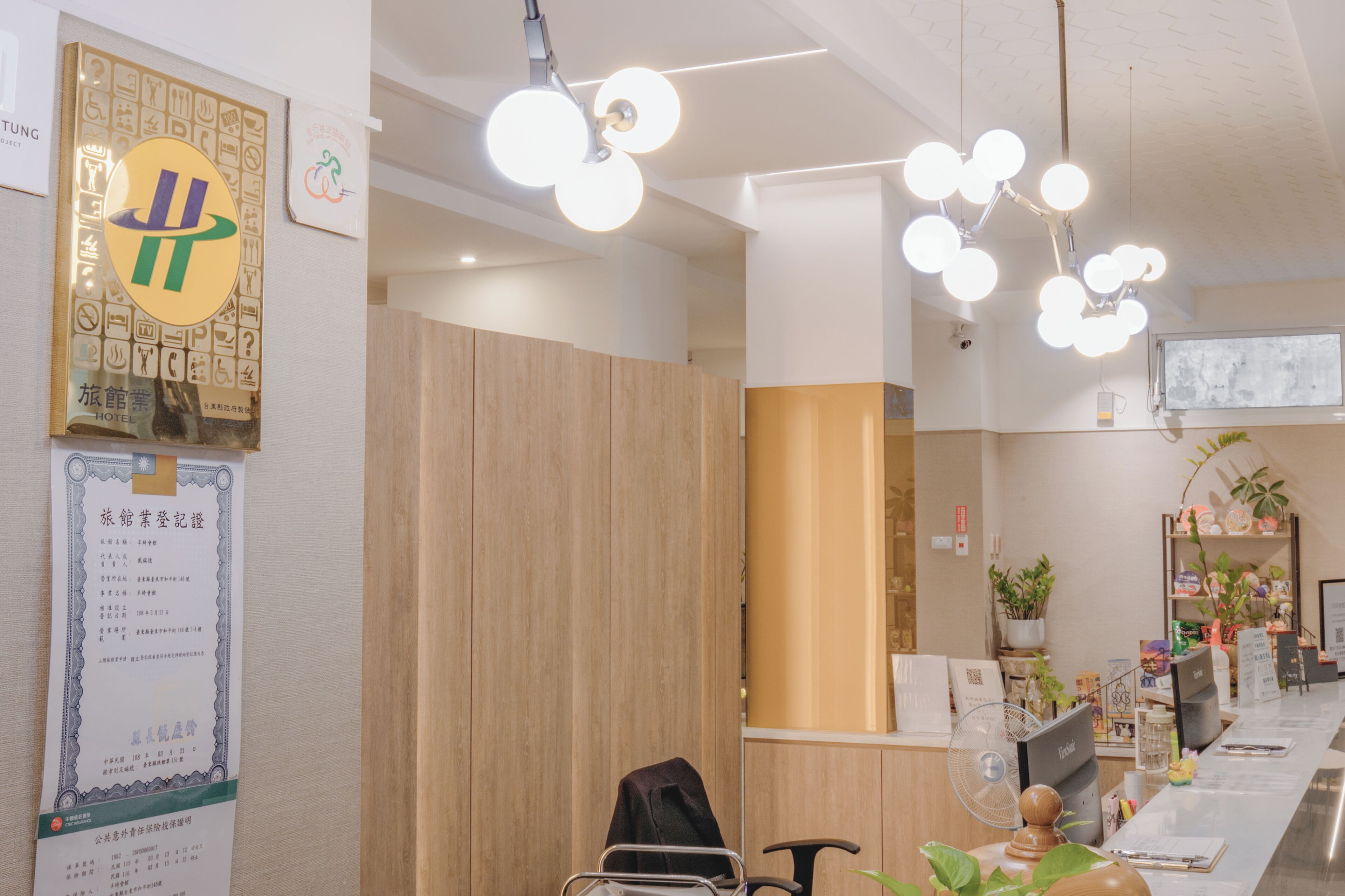 Un espace d’accueil d’hôtel avec un comptoir de réception en bois, un ventilateur et un écran de télévision.