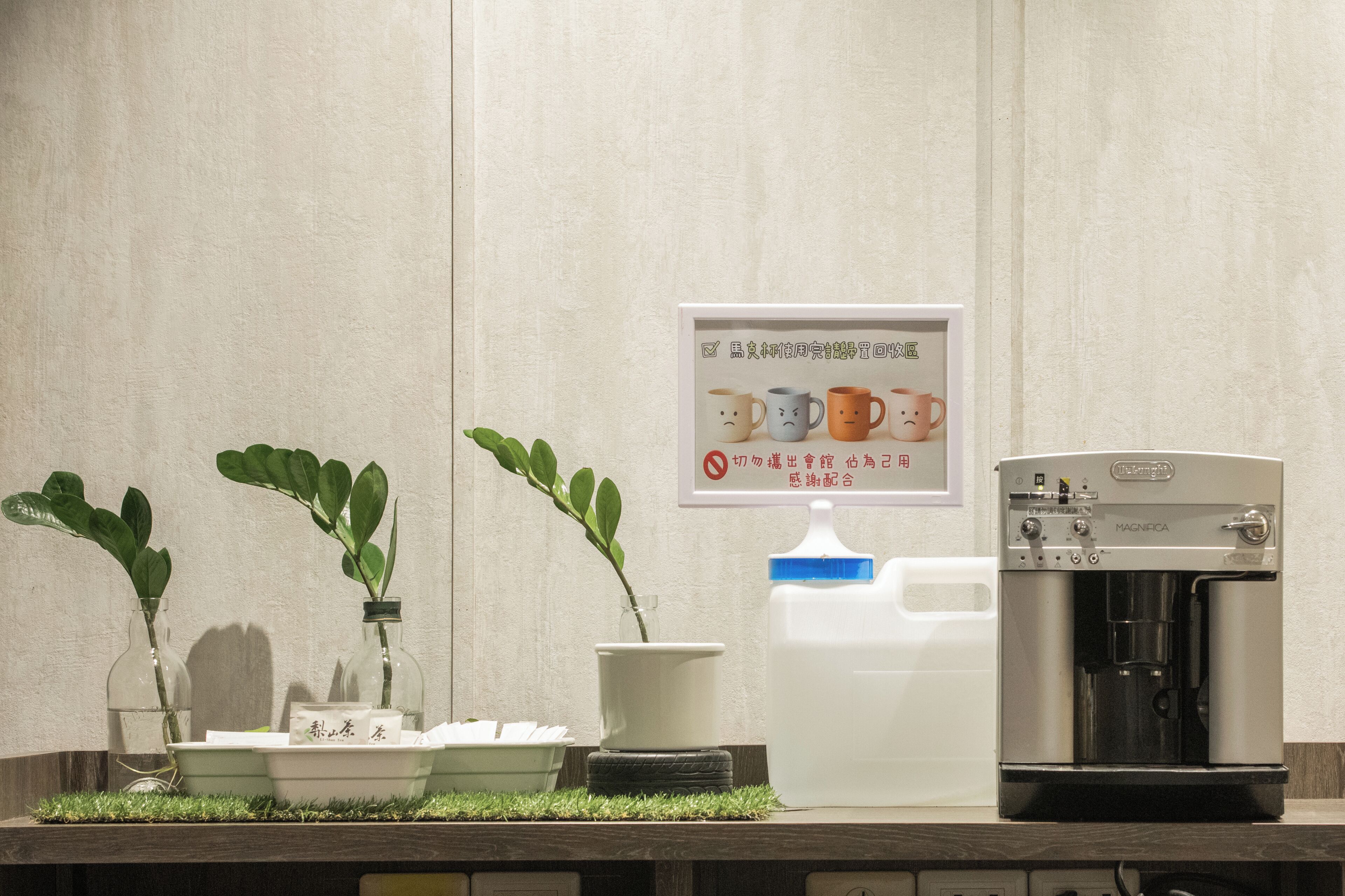 A coffee machine, two potted plants, and a sign on a wall.