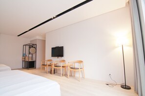 A hotel room with a bed, a desk with chairs, a TV, and a floor lamp.
