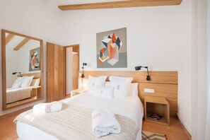 Hotellihuone, jossa on suuri sänky, puinen pääty, yöpöytä, peili ja taulu seinällä.