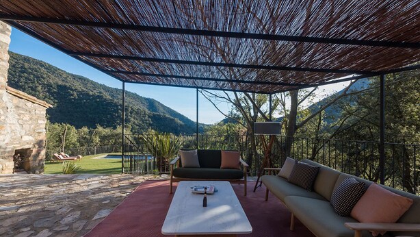 Una veranda esterna con un muro in pietra, una sedia a dondolo, un divano e un tavolo.