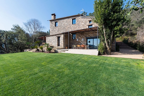 A stone house with a covered patio and a well-maintained lawn.