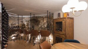 Una cantina vinicola con tavolo e sedie in legno, scaffalature per il vino e un muro in pietra.
