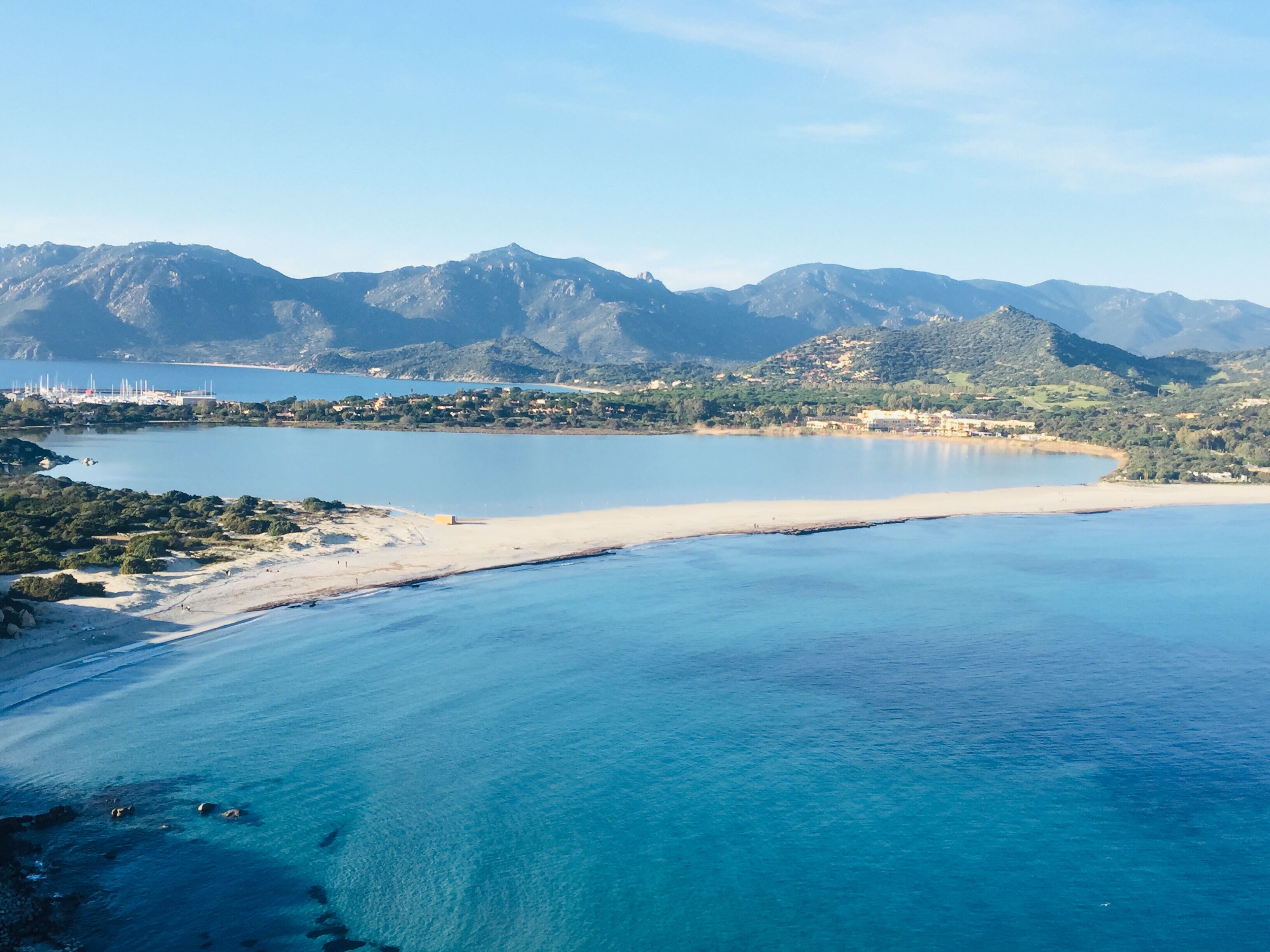 Un paysage côtier avec une plage, une eau d’un bleu limpide et des montagnes en arrière-plan.