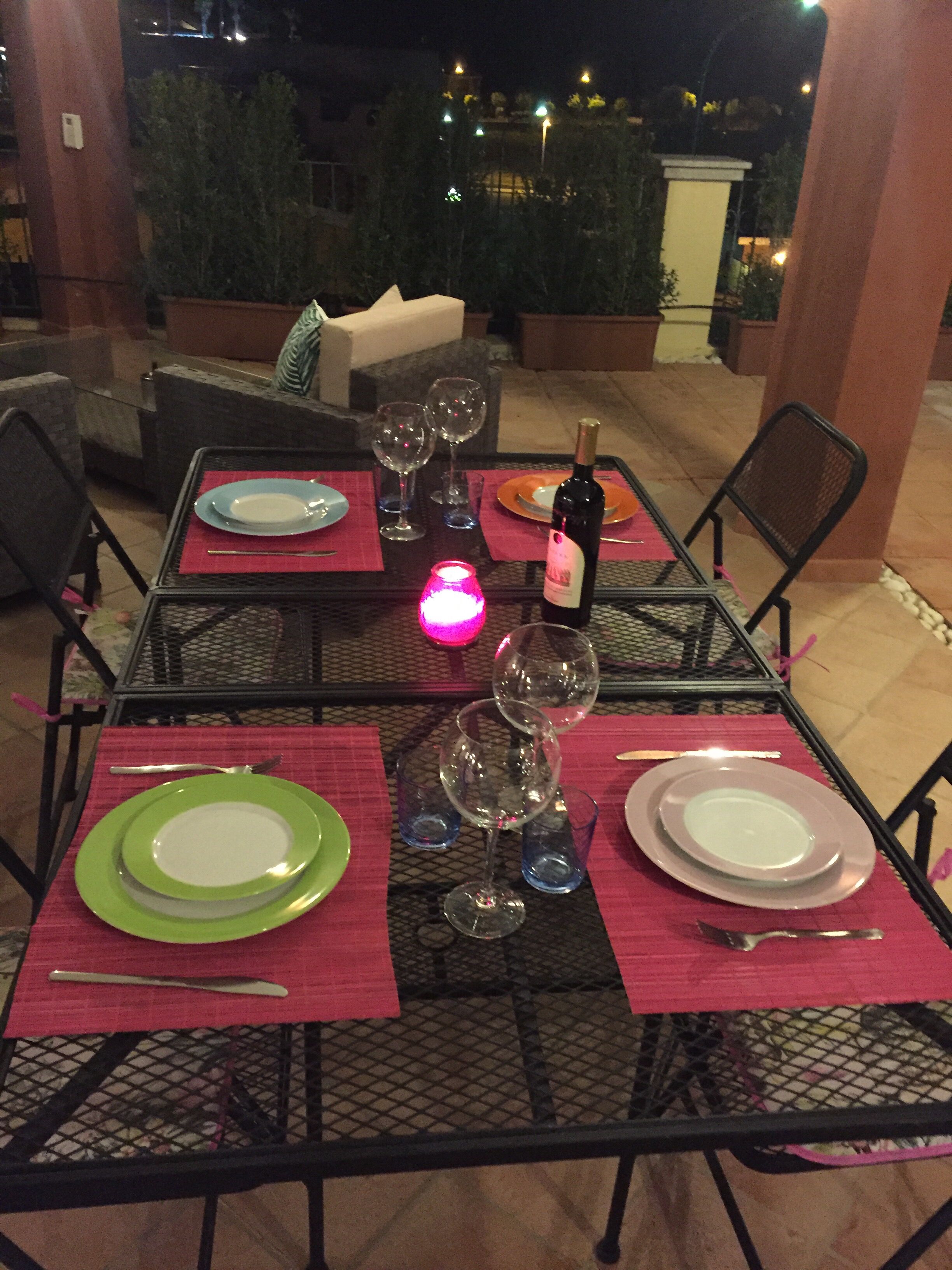 An outdoor dining area with a table set for four, surrounded by chairs, and a bottle of wine on the table.