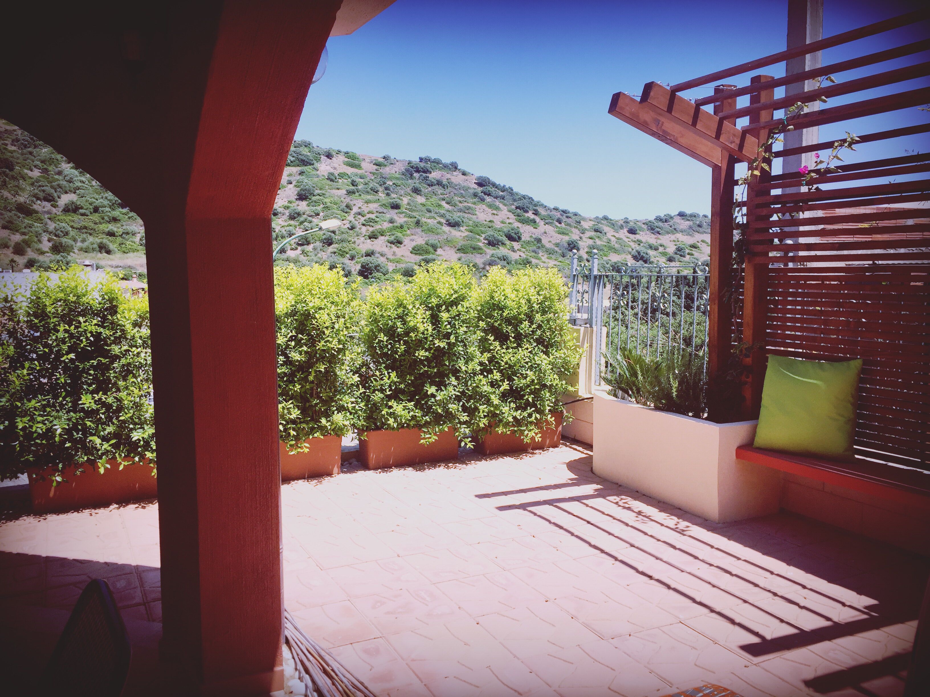 Eine Terrasse mit Blick auf eine hügelige Landschaft, einer Holzpergola und einem grünen Kissen.