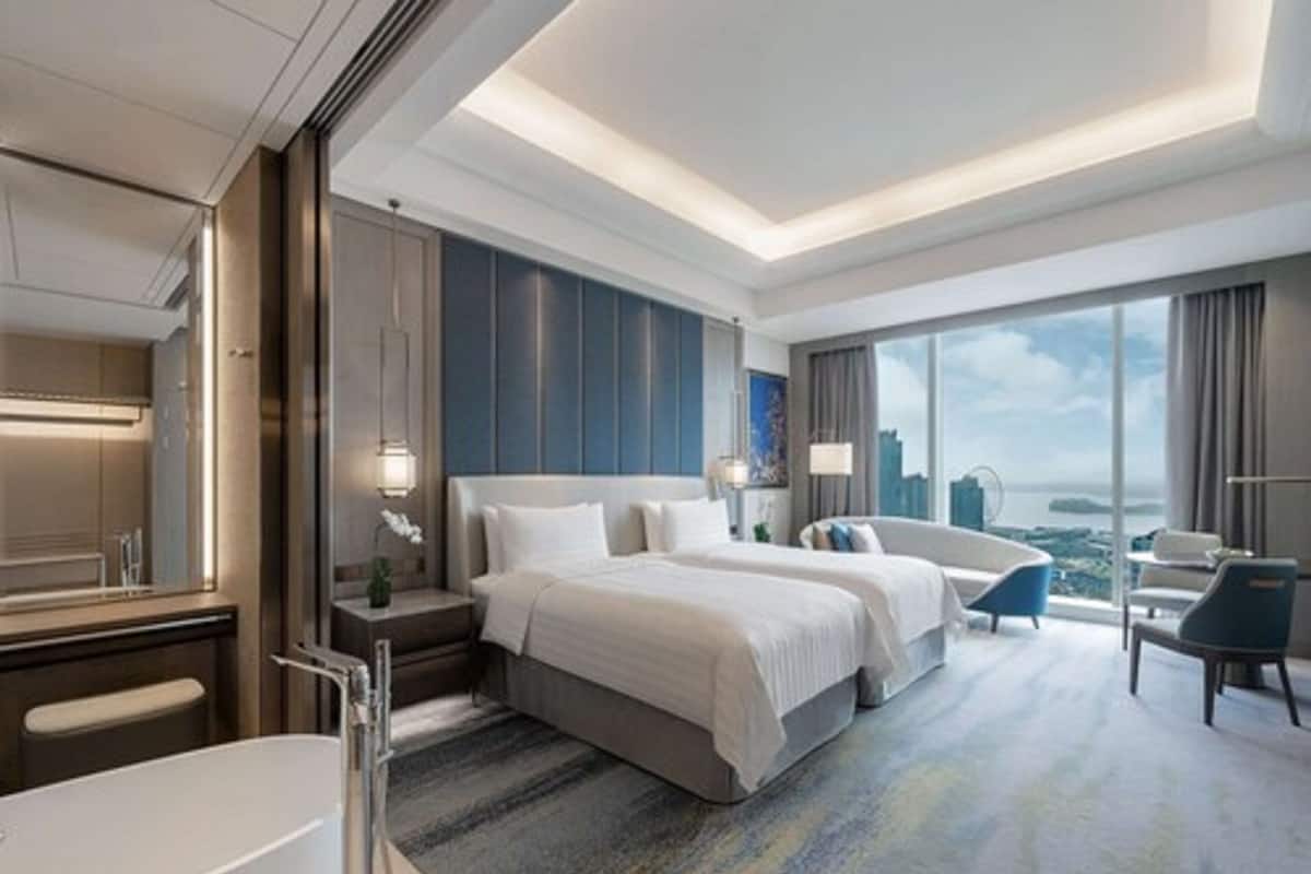 A modern hotel room with a large bed, a separate sofa, a bathtub, and a city view.