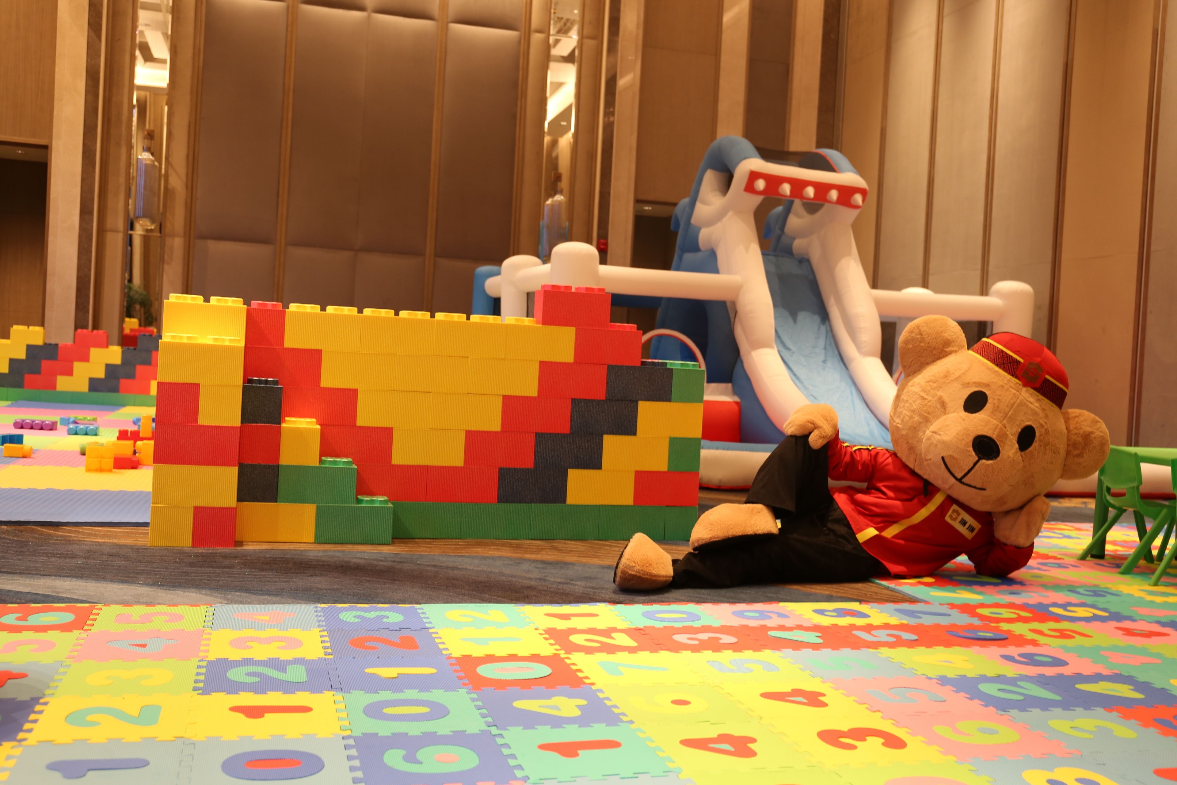 A play area with colorful building blocks, a teddy bear in a red uniform, and a slide.