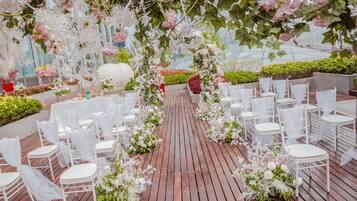A wedding ceremony setup with white chairs and floral decorations on a wooden deck.