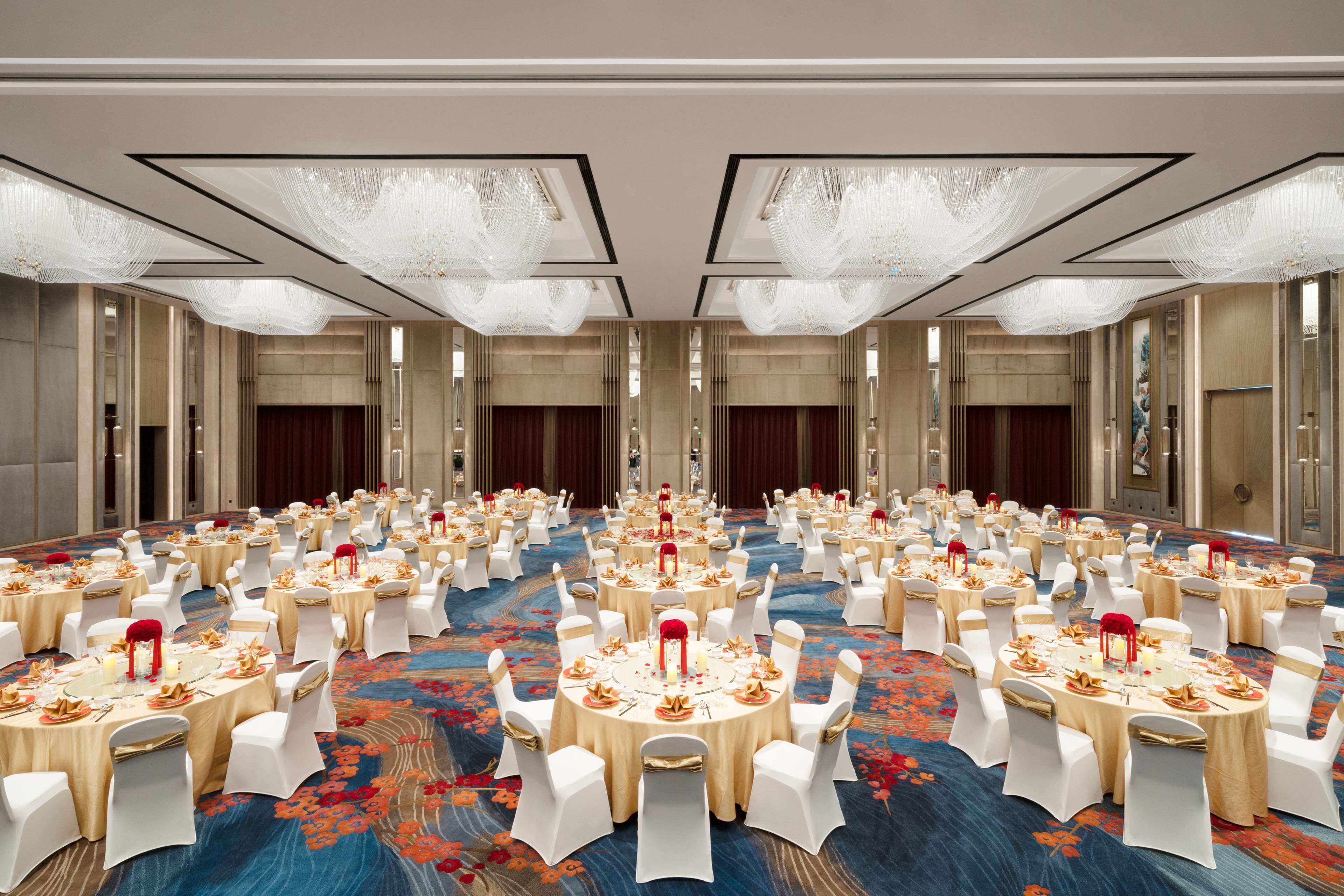 A large banquet hall with round tables, white chairs, and chandeliers.