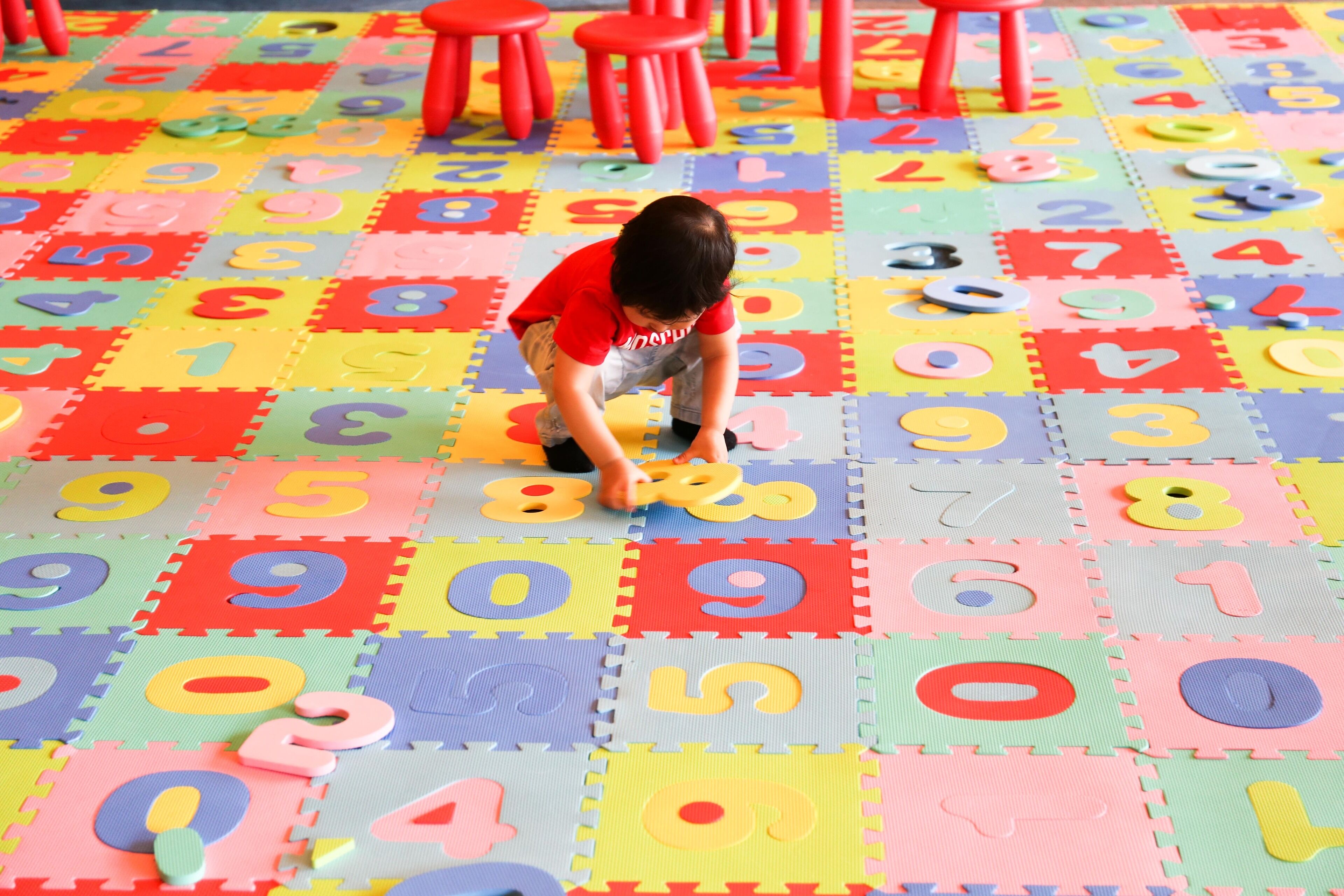 Un niño jugando sobre una alfombra numérica de colores con piezas de puzzle de espuma.