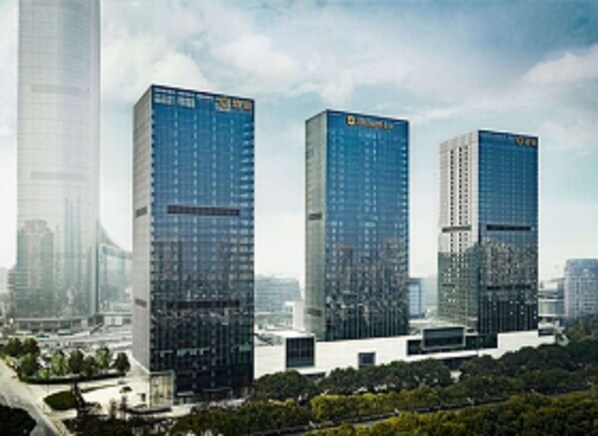A cluster of modern high-rise buildings with reflective glass facades, surrounded by greenery and other urban structures.