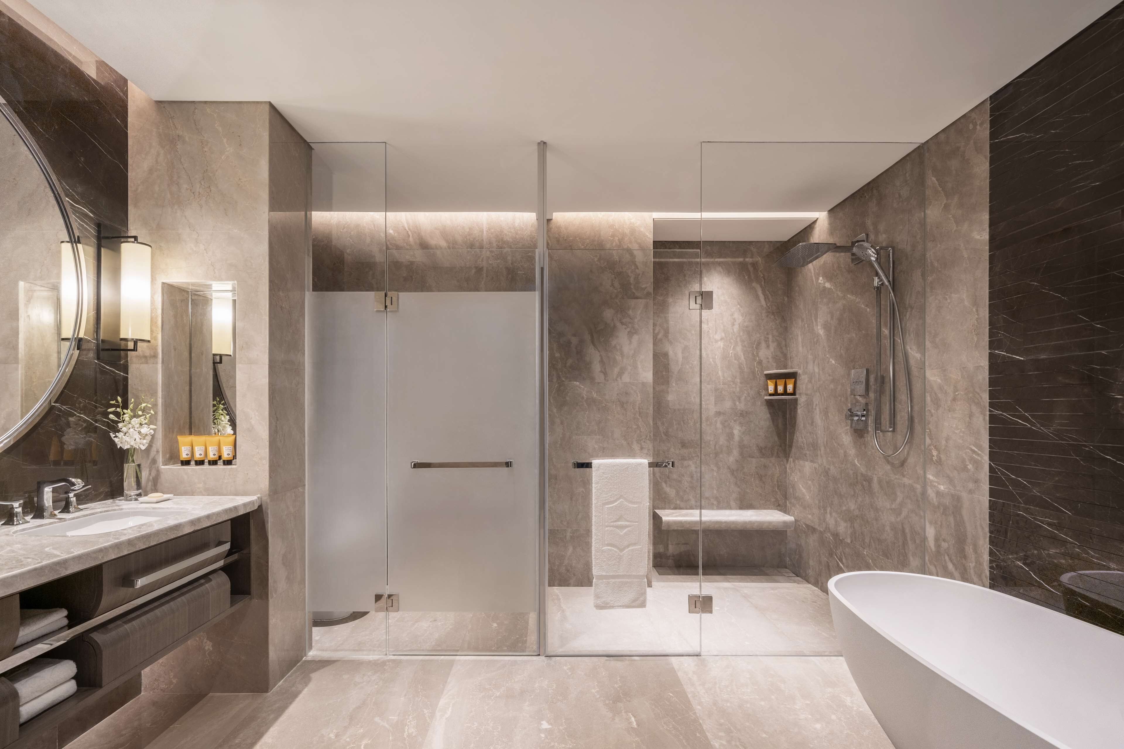 Een moderne badkamer met een douchecabine van glas, een vrijstaand bad en een wastafel met een grote spiegel.
