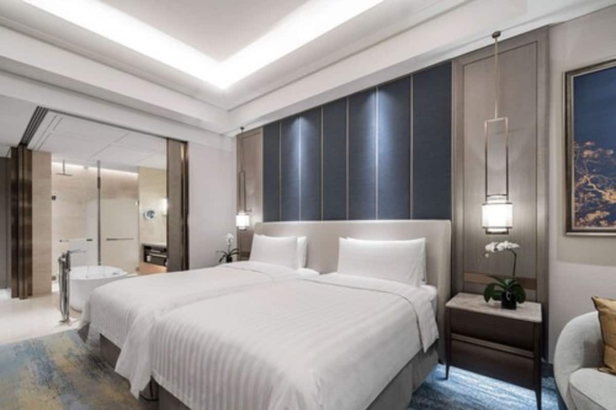 A modern hotel room with a large bed, a bedside table with a lamp, a nightstand, and a view of the city at night.