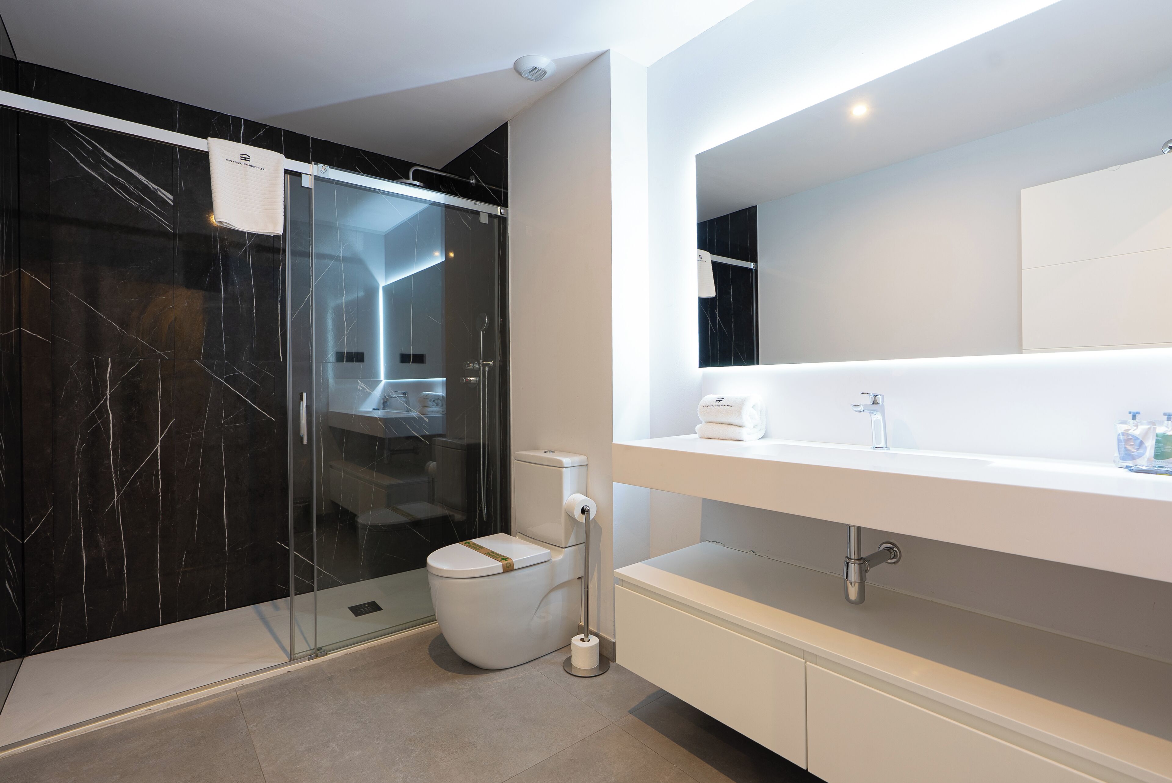 Un baño moderno con ducha envuelta en vidrio, inodoro blanco y un espejo grande sobre un tocador blanco.