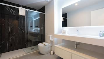 Un baño moderno con ducha envuelta en vidrio, inodoro blanco y un espejo grande sobre un tocador blanco.