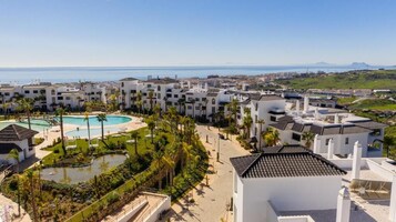 Un resort con varias edificaciones blancas, una piscina central y vista al mar.